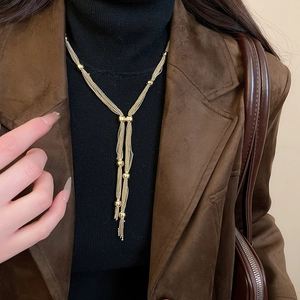 Detailed view of layered gold tassel necklace worn over a black turtleneck sweater