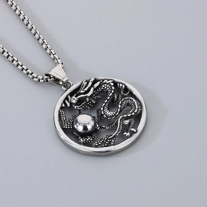 Gros plan d'un pendentif dragon en acier titane avec sculpture de perle sur une chaîne