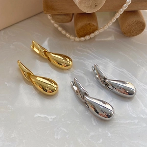 Detailed close-up of gold and silver teardrop earrings on a marble and wooden display