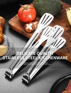 Detailed view of dual stainless steel food tongs on a stone countertop with fresh vegetables