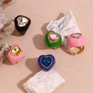 Detail of colorful enamel heart rings with faceted gemstones on textured stone background