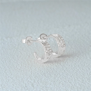 Detail of silver C-shaped earrings with pavé cubic zirconia on a minimalist grey surface