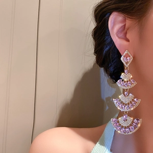 Close-up of fan-shaped tiered gold earrings with purple crystals on a model