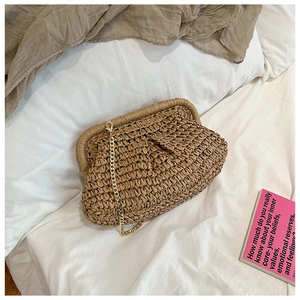 Detail of straw cloud bag with golden chain strap on a soft fabric background