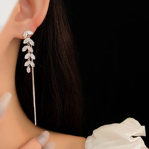 Detail of leaf-shaped silver earrings with sparkling crystals on a model's ear