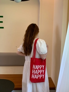 Detail of red canvas tote bag with white HAPPY slogan print and long shoulder strap
