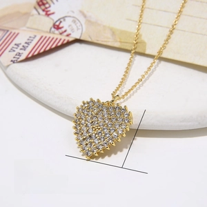 Detail eines Herzanhängers aus Gold mit Zirkonia-Inlay auf einem weißen Steintablett