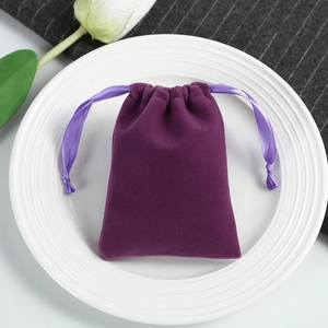 Close-up of purple velvet drawstring pouch on white ceramic plate with green leaves