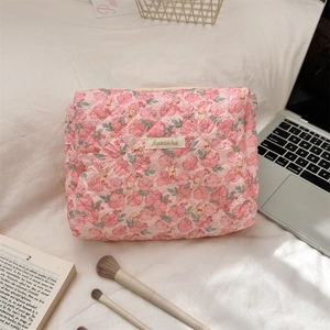 Detail of pink floral quilted makeup bag with zipper closure on a cozy white bed