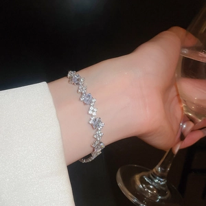 Macro detail of silver zircon oval bracelet on wrist with elegant silk sleeve and glass
