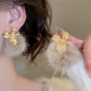 Macro view of gold flower earrings with soft brown plush pom-poms for winter