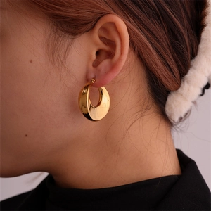 Close-up of thick gold-plated geometric hoop earrings worn by a model in profile