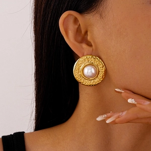 Close-up of vintage golden textured metal earrings with large pearls worn by a model