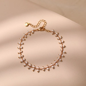 Detail of bohemian gold link chain bracelet with white cylindrical beads and lobster clasp