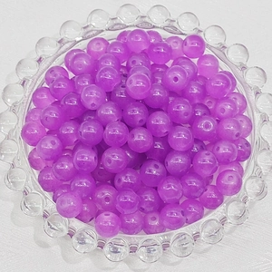 Close-up of translucent purple glass beads on a decorative glass tray for DIY jewelry