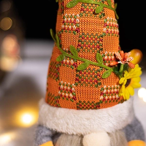 Knitted autumn gnome doll with orange plaid hat and sunflower decoration in warm light