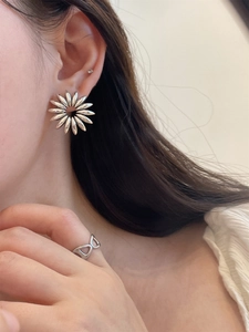 Close-up of silver petal earrings and geometric hollow ring on a model's ear and hand
