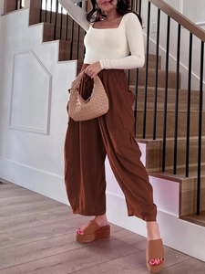 Pantaloni larghi marroni in lino con top bianco panna e borsa intrecciata a mano