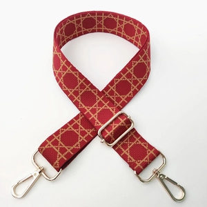 Detail of red woven bag strap with adjustable golden hardware on white background