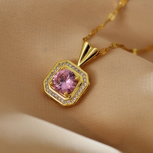 Macro shot of square gold necklace pendant with pink gemstone and small clear crystals