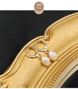 Close-up of golden hoop earrings featuring natural white baroque pearls on vintage frame