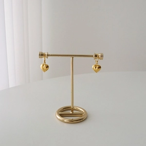 Detailed view of gold heart drop earrings displayed on a minimalist jewelry stand