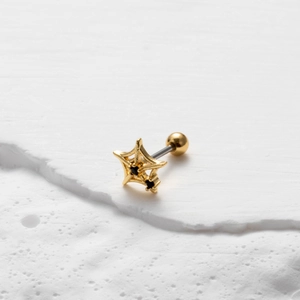 Dettaglio di piercing a stella dorata con zircone nero su superficie bianca testurizzata