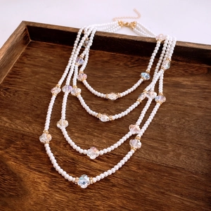 Detail of multi-layer pearl necklace with flower accents and gold hardware on wood
