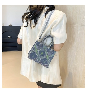 Rear view of a blue denim handbag with green star patterns and frayed fringe edges