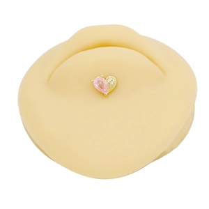 Macro detail of heart-shaped belly ring with pink zircon and gold engraved texture
