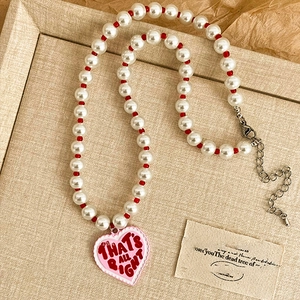 Detail of pearl choker with red beads and pink heart enamel pendant inscribed with text