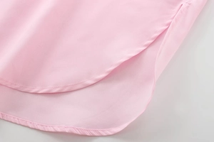 Détail d'une chemise en coton rose montrant l'ourlet arrondi et les fentes latérales
