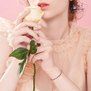 Close-up of a colorful zircon tennis bracelet on wrist next to a yellow rose flower