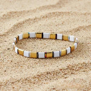 Detail of bohemian flat beaded elastic bracelet with gold and white accents on sand