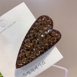 Detailed close-up of heart-shaped hair clip with amber rhinestones on display card