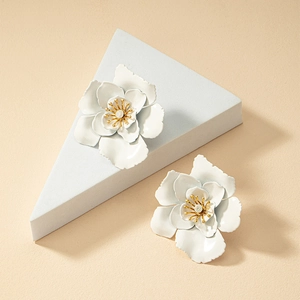 Detailed view of matte white layered flower earrings with golden stamen on textured background