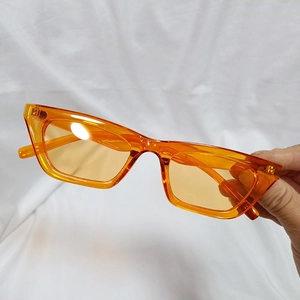 Detail view of orange transparent narrow rectangle sunglasses held against a white fabric