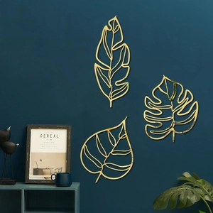 Détail de trois décorations murales en fil métallique doré aux formes de feuilles de monstera