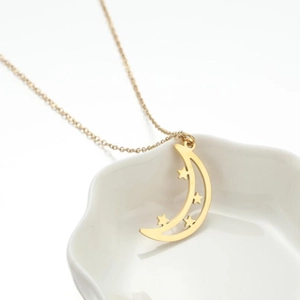 Detail of gold crescent moon pendant necklace with star cutout in a ceramic dish