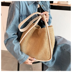 Detail of hand-woven straw tote bag featuring premium cream leather handles and trim