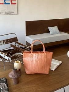 Detailed view of the orange straw woven tote bag texture and dual handles on a wooden table