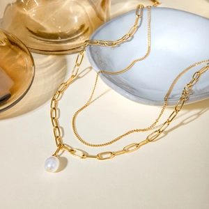 Detail of layered gold paperclip chain and thin necklace with elegant white pearl