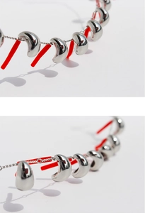 Macro shot of silver bean pendants and red elongated accents on a minimalist necklace