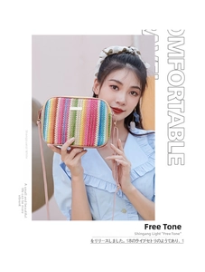 Detail of a rainbow striped woven straw crossbody bag with metallic logo and pink leather strap