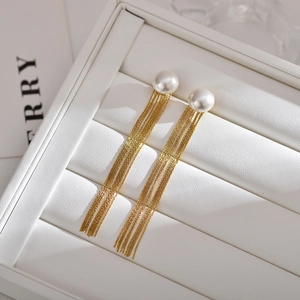 Detail of long gold tassel earrings with round pearls on a white jewelry display