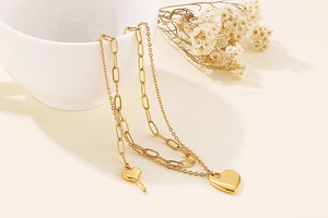 Detail of double-layered golden heart necklace with paperclip chain and key pendant
