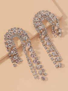 Detail of silver crescent moon fringe earrings with shimmering crystals on a beige stand