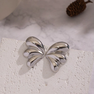 Macro detail of silver butterfly wing earrings on a textured stone surface display