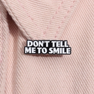 Detail of 'DON'T TELL ME TO SMILE' black enamel pin badge on pink denim jacket