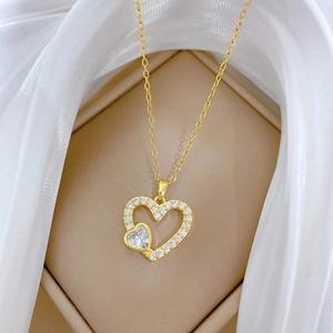 Élégant collier doré à double pendentif cœur avec cristaux dans un écrin à bijoux beige